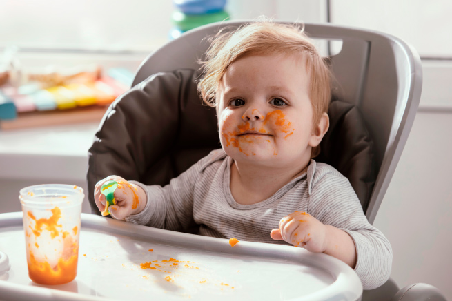 Child eating with orange puree on the face
